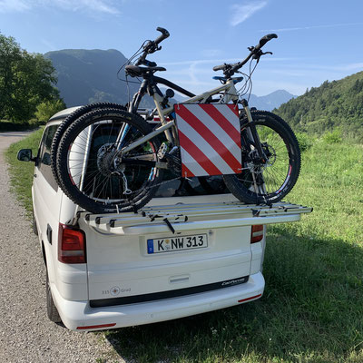 Achterkant van een witte VW California met bagage op een groen veld