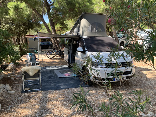 Vue de face de notre VW Bulli blanc avec des chaises sous l'auvent déployé au Camping Village Šimuni