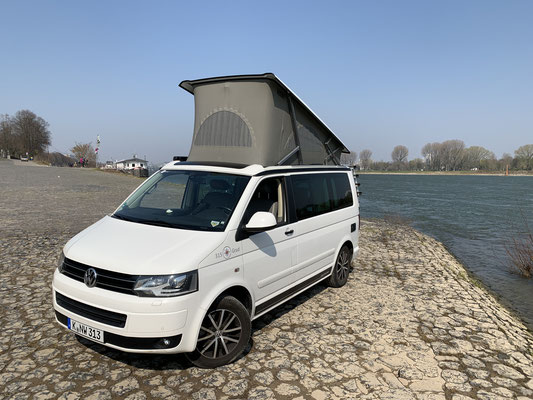 White T5 California with raised high roof on the Rhine near Cologne