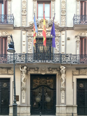 Fassade eines Bankgebäudes mit Balkon, welcher von Kipsfiguren gestützt wird. 