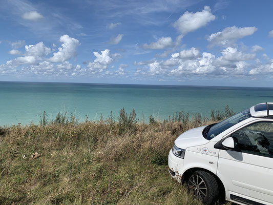 VW T5 California bianco sul bordo delle scogliere in Normandia, con una vista mozzafiato sul mare