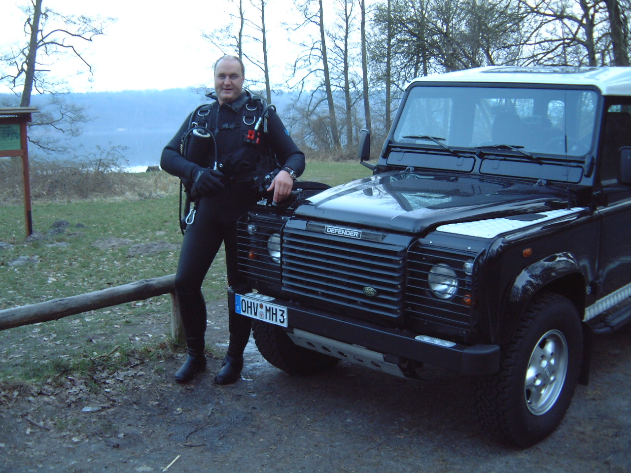 Glücklicher Taucher am Werbelinsee vor schwarzem Land Rover Defender